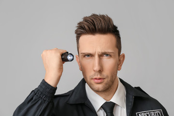 Male security guard with flashlight on grey background