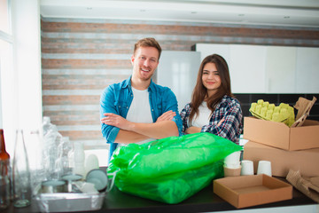 Couple sorts trash in the kitchen. Waste must be sent for recycling. There are a lot of recyclables. On the table are plastic, glass, iron, paper, old Electrical appliances and biodegradable waste.