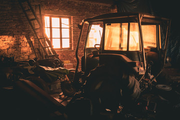 Fototapeta na wymiar Old disassembled tractor in a brick workshop at sunset. The rays enter the building