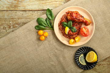 Chicken legs with red rice in tomato-garlic sauce on a plate on a wooden table on a linen tablecloth tomato and lemon.