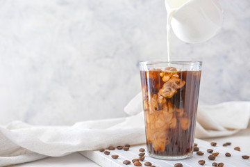 Pouring of milk into cold coffee in glass on table