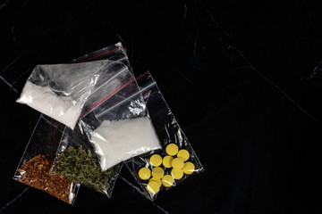lethal concept: tobacco, weed, MDMA tablets, amphetamine crystals, heroin in plastic bags, on a dark background. Enhanced contrast, partial blur.