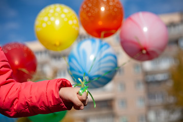 Bright sunny day. A girl holds balloons filled with helium. Defocus on the balls. Horizontal frame. Color photo.