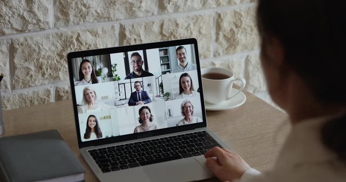 Group business video chat concept. Over shoulder closeup view of female remote employee and office team communicating during virtual meeting by web cam online digital conference on laptop screen.