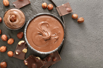 Bowls with tasty chocolate paste and hazelnuts on grey background