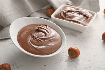 Bowls with tasty chocolate paste and hazelnuts on light background