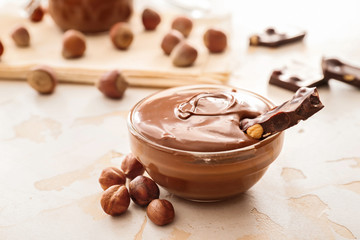 Bowl with tasty chocolate paste and hazelnuts on light background