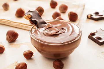 Bowl with tasty chocolate paste and hazelnuts on light background