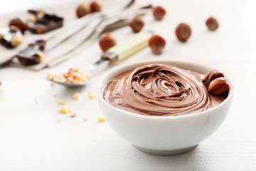 Bowl with tasty chocolate paste and hazelnuts on white wooden background