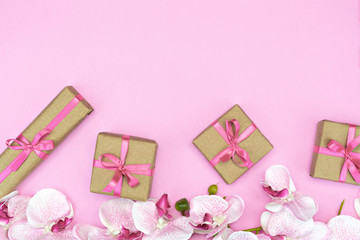 flatlay of Gift present boxes with pink ribbon, orchid flowers on pink background. Copy space