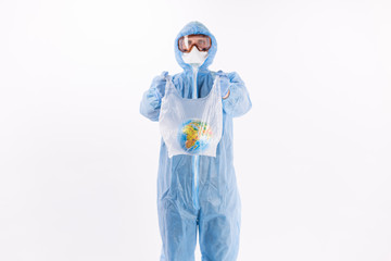 portrait of a man in a chemical protection suit, medical gloves, a mask and glasses holds a package with the planet Earth inside on a light background