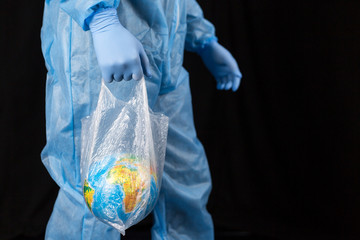 a man in a chemical protection suit and medical gloves holds a package in his hands with a planet inside, a pandemic in the hands of a man. Save the nature. close-up on a dark background