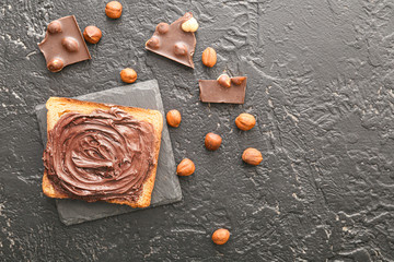 Fresh bread with chocolate paste and hazelnuts on dark background