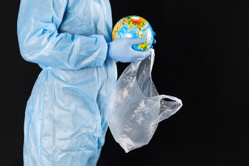 a man in a chemical protection suit and medical gloves holds a package in his hands with a planet, a pandemic in the hands of a man. Save the nature. close-up with place for text on a dark background