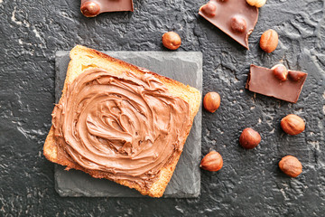 Fresh bread with chocolate paste and hazelnuts on dark background
