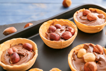 Tartlets with tasty chocolate paste and hazelnuts on tray, closeup