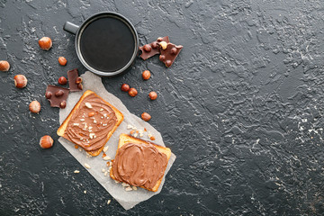 Fresh bread with chocolate paste and cup of coffee on dark background