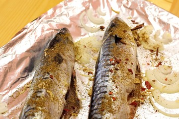 Mackerel fish is ready for baking. Fish is showered with tasty and aromatic seasonings and folded on foil.