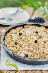 Rustic cake with berries on the wooden table outdoors. Tart filled with blueberries with crumble topping made of walnuts, oats and butter.