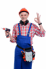 Photo of senior male, professional worker in blue uniform with electric drill, show okay sign isolated on white background