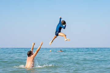 Father, playing with children at the seaside. Executing water jumps. Boy flying in midair.