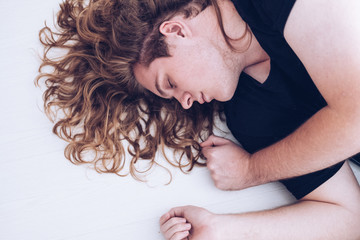 view of young man with blond curly long hair, eyes closed lying down