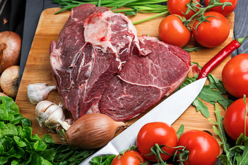 The preparation of fresh meat. Fresh beef steak on a wooden table. Meat surrounded by spices and vegetables. Fresh fruit. Red ripe tomatoes. Dietary food.