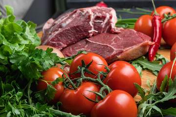 A piece of raw meat on a wooden cutting Board and various vegetables. Cooking meat. Fresh beef and ripe vegetables. Balanced diet. Natural protein.
