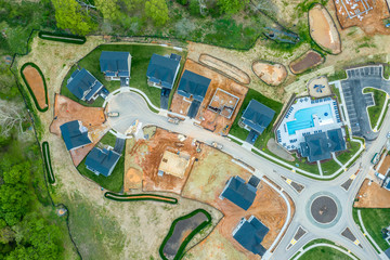 High resolution aerial picture of a new American residential real estate development single family homes built, under construction and home sites for sale, traffic circle, community pool
