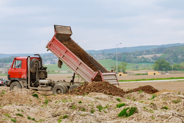 Dump truck unloading soil at construction site.