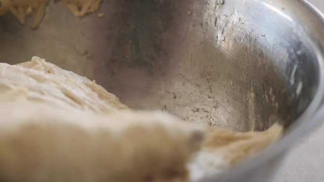 Stirring homemade bread dough in a metal bowl. A home baker stirs raw sourdough batter with a wooden spoon forming gluten. Baking bread during the 2020 lockdown is the current trending hobby.