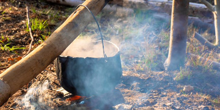steaming old pot outdoor. cooking and camping. outdoor adventures concept. beaten cauldron on camp fire