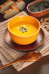 Roasted pumpkin and carrot soup with cream and pumpkin seeds on a wooden table..