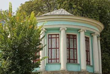 old round historical building with white columns, a blue wall and large windows overgrown with green vegetation on the street