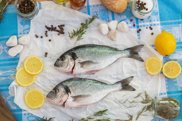 Two fresh breams on a baking paper with lemons and herbs