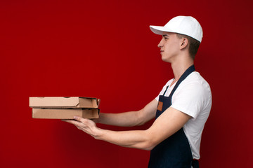 pizza delivery man in uniform on a red background gives boxes of food, the courier guy gives the finished order