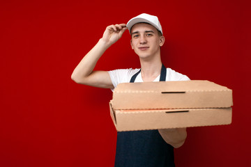 pizza delivery man in uniform on a red background gives boxes of food, the courier guy gives the finished order