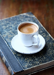 Cup of coffee and old book on rustic background.  