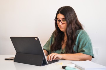 Young spanish brunette wearing glasses teleworking with her hybrid tablet laptop adapting her...
