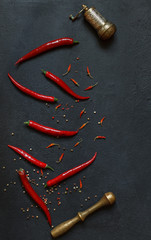 Red pepper pods, dried baby paprika and pepper peas with copper cooking utensils on a black table top, vertically