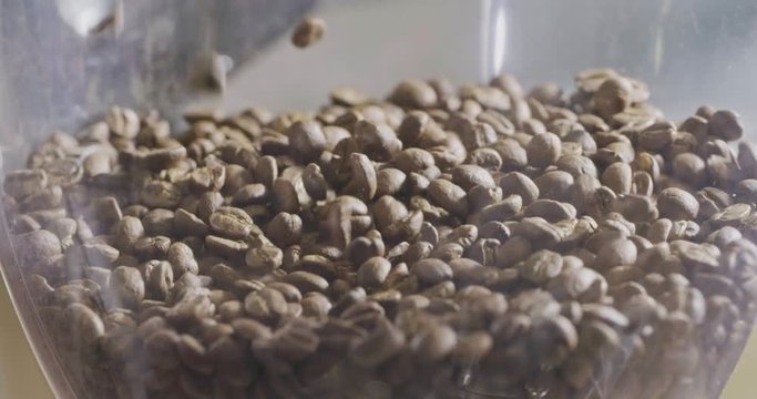 Close-up video of aromatic roasted coffee beans pour into a coffee grinder.