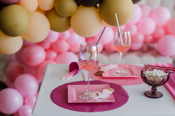 Festive table setting in pink colors, white plates, glasses with cocktail sticks. Colorful balloons decoration. Birthday, baby shower or girls party.