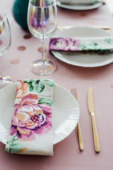Guest place, table setting in dusty pink colors with beautiful white dishes, golden cutlery, confetti, glasses of wine. Close up. elective focus.