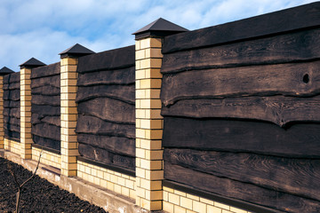 Strong wooden fence with brick posts Horizontal boards are tightly nailed to each other and provide reliable protection from robbers. A symbol of safety.