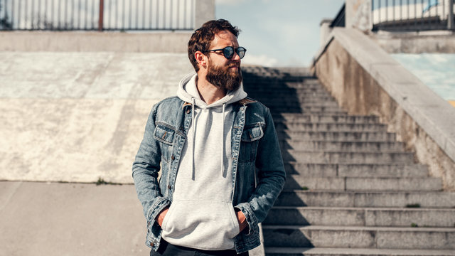 City portrait of handsome hipster guy with beard wearing gray blank hoodie or hoody with space for your logo or design. Mockup for print