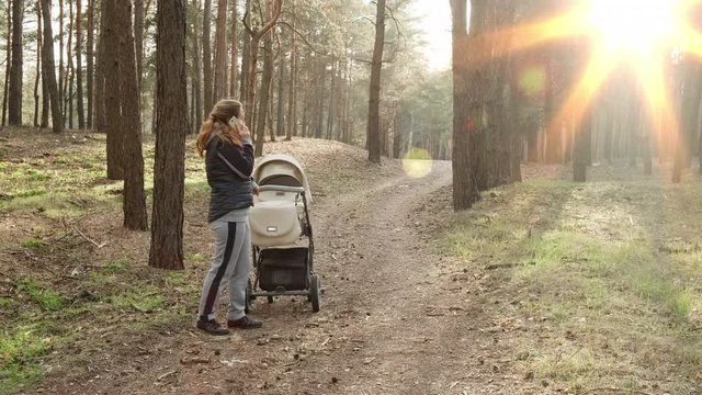 A woman with a stroller walks in the spring forest in the fresh air and is not afraid of viruses. Mom walks in the woods with a small child and talks on the phone. 4K UHD video camera, 2x slow motion.
