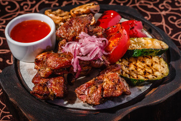 Wooden plate with meat, roasted vegetables and sauce.