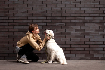 young guy sits with a retriever puppy on the street against the background of the wall and kisses him, a man caresses and kisses a dog