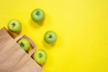 Ripe green apples and eco friendly paper bag on yellow background, copy space, top view. Natural products for healthy food and diet, fitness nutrition.