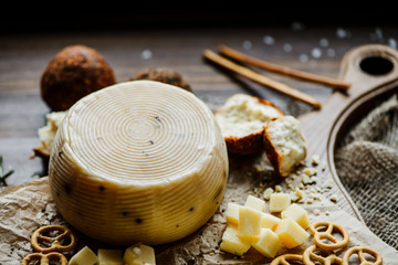 Round cheese with pretzels and snacks on the cutting Board. On a wooden background. Selective focus.
